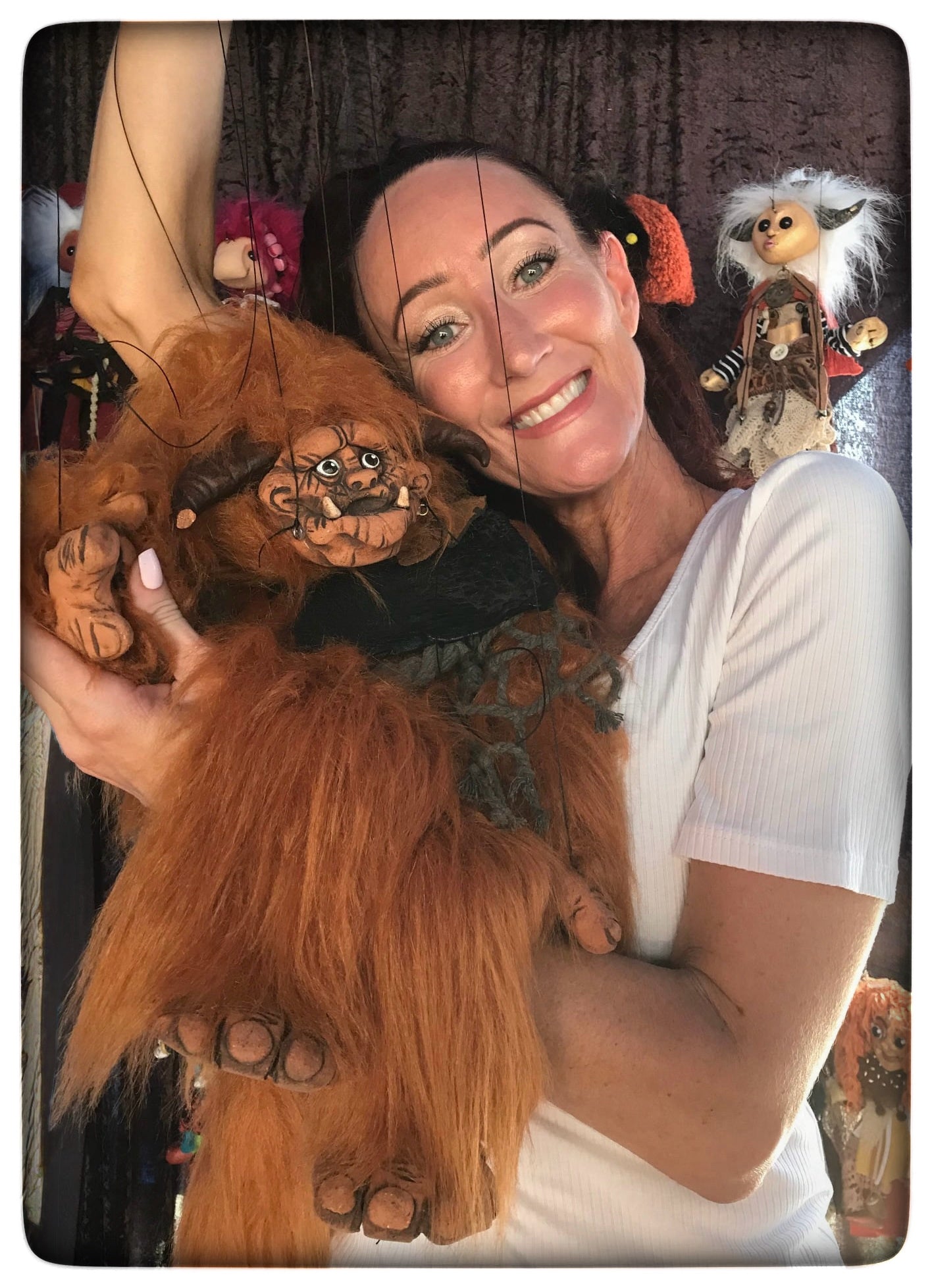 Woman holding a large furry puppet with various puppets in the background