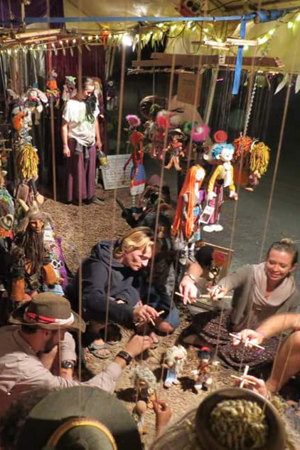 People in a market or fair setting with colorful costumes and decorations.